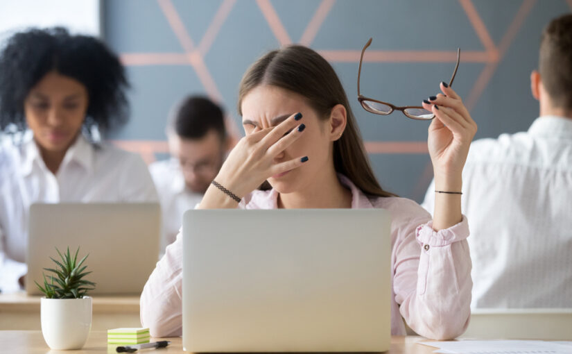 A woman at work on a computer rubs her eyes in discomfort from the digital strain on her eyes